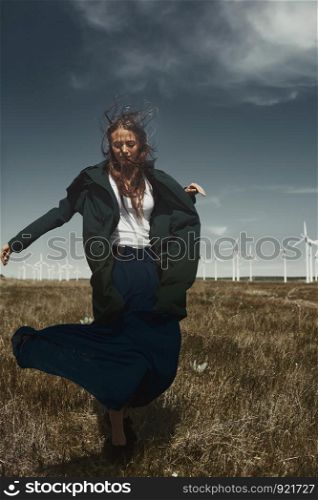 Woman with long tousled hair next to the wind turbine with the wind blowing
