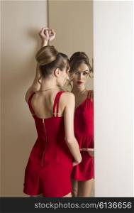 woman with make-up and hair-style trying elegant red dress in changing room in front of mirror