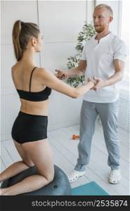 woman with male physiotherapist doing exercises with ball