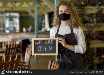 woman with mask holding chalkboard with open sign