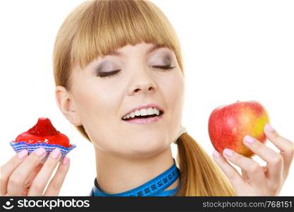Woman with measuring tape holds in hand cake and apple fruit choosing, trying to resist temptation, make the right dietary choice. Weight loss diet dilemma gluttony concept. Isolated on white. Woman choosing fruit or cake make dietary choice