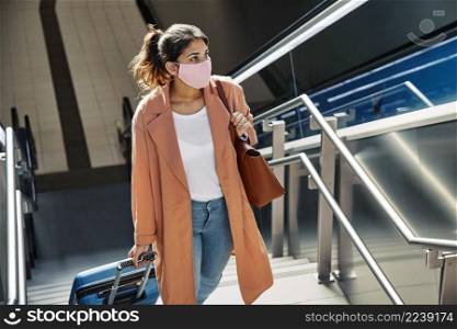 woman with medical mask luggage climbing stairs airport during pandemic