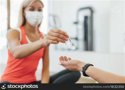 woman with medical mask offering hand sanitizer person gym