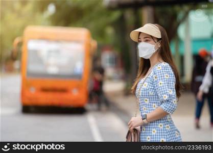 woman with medical mask to protect coronavirus covid-19  while waiting bus at bus stop in the city