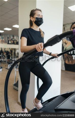 woman with medical mask using gym equipment