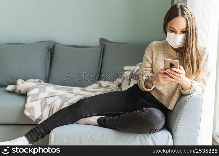 woman with medical mask using her smartphone home during pandemic
