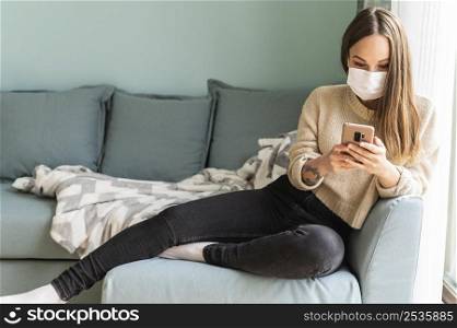 woman with medical mask using her smartphone home during pandemic