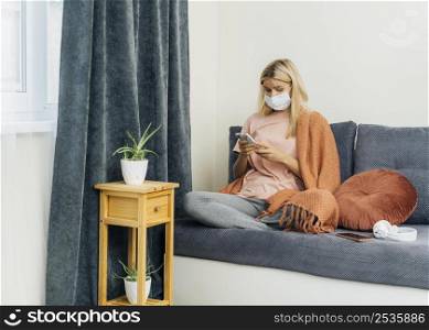 woman with medical mask using smartphone home during pandemic