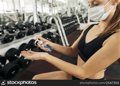 woman with medical mask working out gym using hand sanitizer