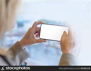 Woman with modern mobile phone in hands touching on a blank screen. Blurred office interior on a background.