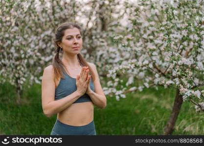 Woman with namaste yoga mudra hands on spring blossom garden natural background. Healthy girl training at outdoors. Gratitude, unity with nature, peace and love concept. High quality photo. Woman with namaste yoga mudra hands on spring blossom garden natural background. Healthy girl training at outdoors. Gratitude, unity with nature, peace and love concept.