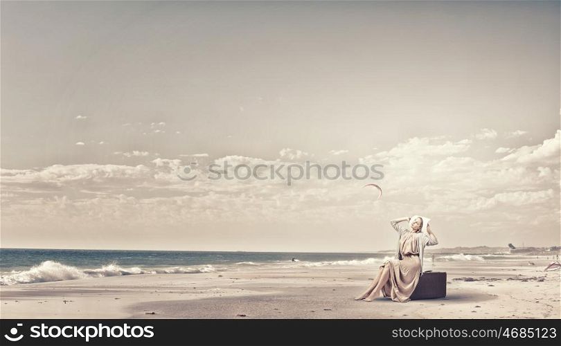 Woman with old suitcase. Beautiful woman sitting on retro suitcase on sea coast