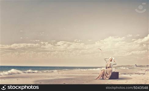 Woman with old suitcase. Beautiful woman sitting on retro suitcase on sea coast
