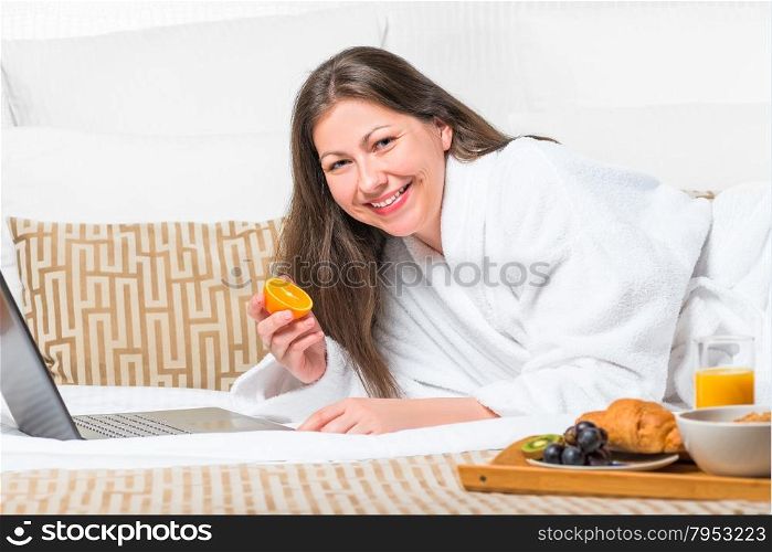 woman with orange in her hand on the bed in the morning working