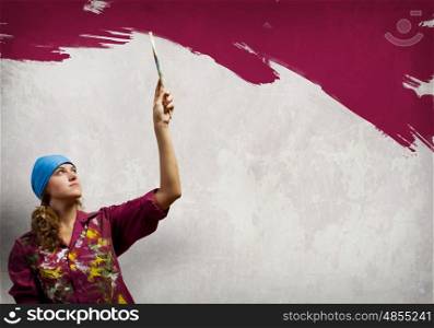 Woman with paintbrush. Young woman painting wall in colors with brush
