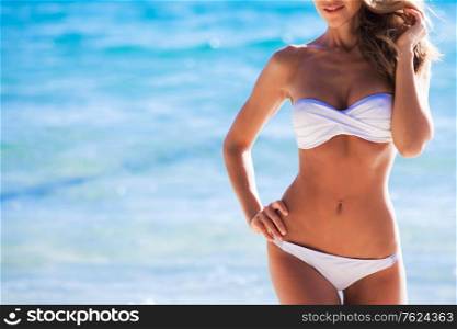 Woman with perfect body in white bikini posing on sea background. Woman in bikini on sea background