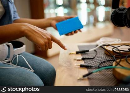 Woman with phone choosing headphones in speaker systems store, music fan. Female person in audio shop, showcase with earphones on background, buyer in multimedia salon. Woman with phone choosing headphones in store