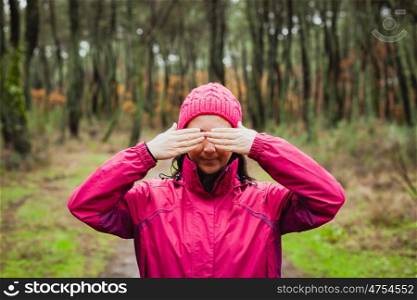 Woman with pink wool hat in the forest covering her eyes