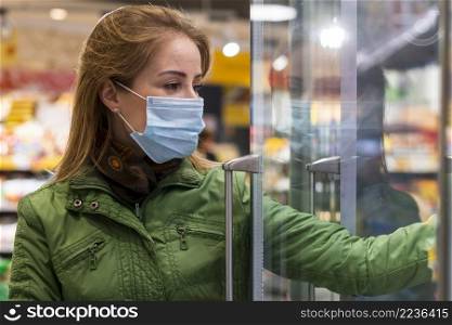 woman with protective mask taking products from fridge