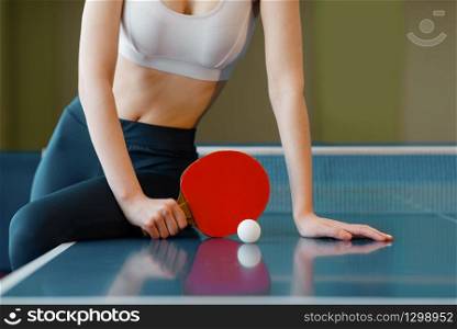 Woman with racket and ball poses at the ping pong table indoors. Female person in sportswear, training in table tennis-club. Woman with racket poses at the ping pong table