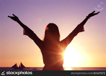 Woman with raised hands at sunset by the sea. Woman at sunset by the sea