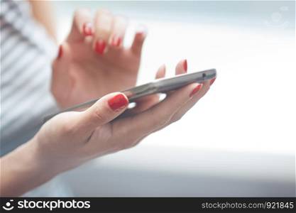Woman with red manicure using smartphone. Horizontal photo