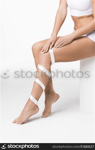 Woman with ribbon on leg. Studio shot of young woman with perfect body with leg wrapped in white ribbon, depilation, varicose concept