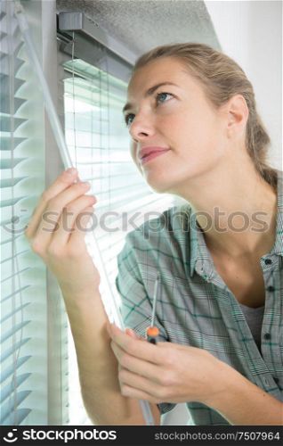 woman with screwdriver adjusting window blind