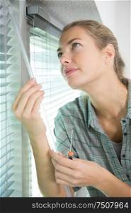 woman with screwdriver adjusting window blind