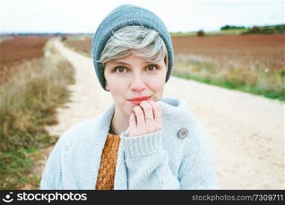 Woman with short and gray hair is alone in the beggining of a rural path in a cold autumn day