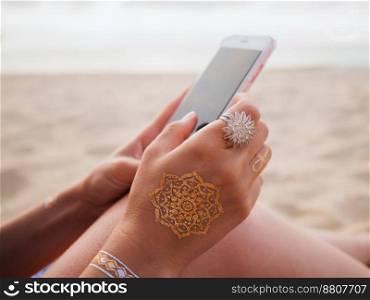 Woman with smartphone on beach. Hands of young girl with flash tattoo using mobile device. High quality photo. Woman with smartphone on beach. Hands of young girl with flash tattoo using mobile device.