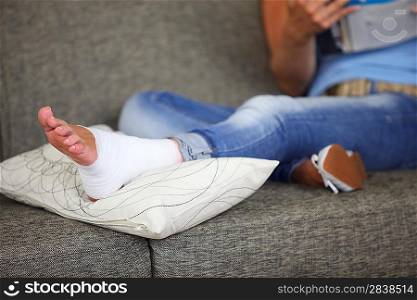Woman with sprained ankle reading on the sofa