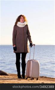 Woman with suitcase is traveling at sea coast in winter