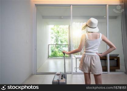Woman with suitcase near door room apartments or hotel hall interior.