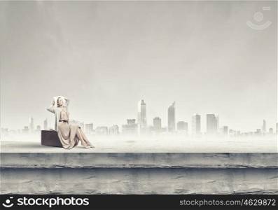 Woman with suitcase. Woman in long dress and hat sitting on retro suitcase