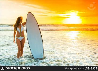 Woman with surfboard. A beautiful young slim sporty woman in bikini with a surfboard is standing at ocean beach at sunset