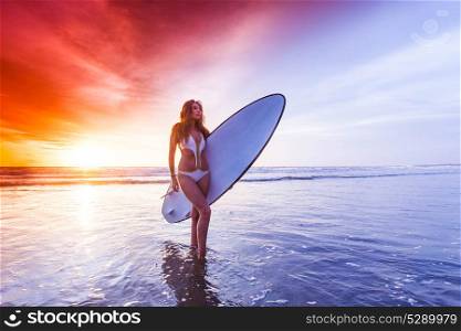 Woman with surfboard. A beautiful young slim sporty woman in bikini with a surfboard is standing at ocean beach at sunset