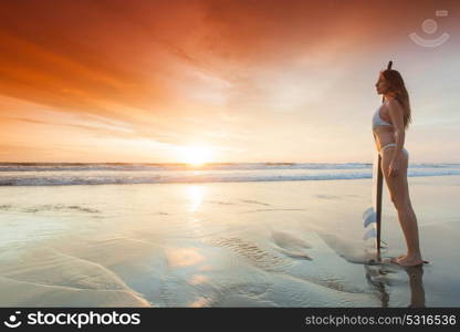 Woman with surfboard. A beautiful young slim sporty woman in bikini with a surfboard is standing at ocean beach at sunset