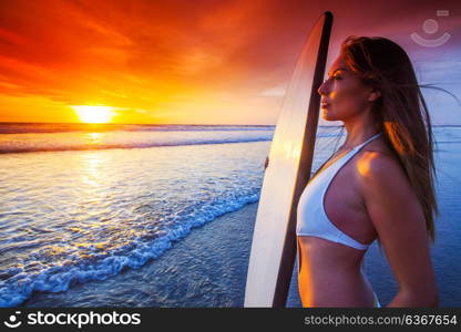 Woman with surfboard. A beautiful young slim sporty woman in bikini with a surfboard is standing at ocean beach at sunset