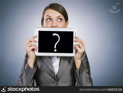 Woman with tablet. Beautiful young woman holding tablet with question against her mouth