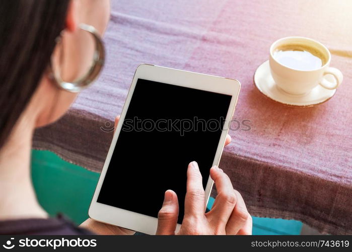 Woman with tablet in hand and cup of coffee on table.