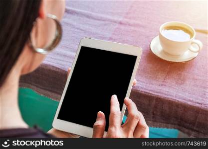 Woman with tablet in hand and cup of coffee on table.