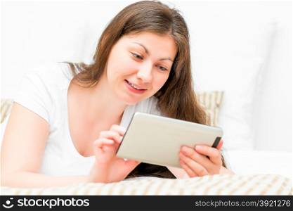 woman with tablet resting on a bed in a bedroom