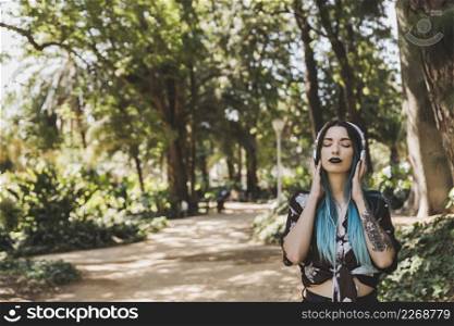 woman with tattoo her hand enjoying music headphone standing park