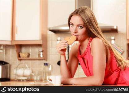 Woman with tea coffee eating gingerbread cookie.. Pretty woman with tea or coffee eating heart shape gingerbread cookie. Gorgeous young girl with hot beverage relaxing in kitchen.
