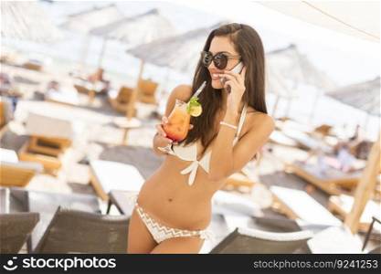 Woman with the drink on the phone at the beach