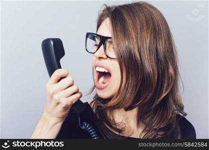 Woman with the office or home phone swears, screams. On a gray background.