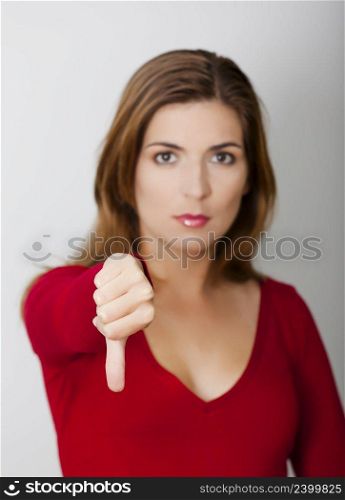 Woman with thumbs down against a gray wall, focus on the hand