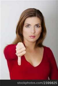 Woman with thumbs down against a gray wall, focus on the hand