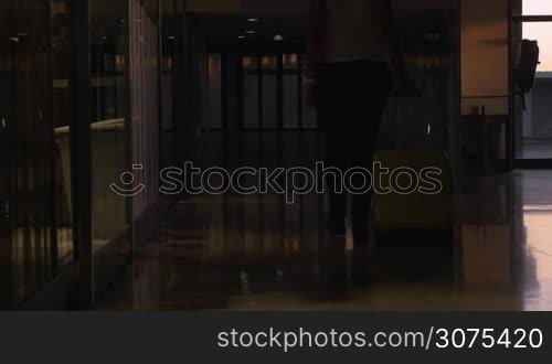 Woman with travel bag walking in the terminal of airport at sunset time